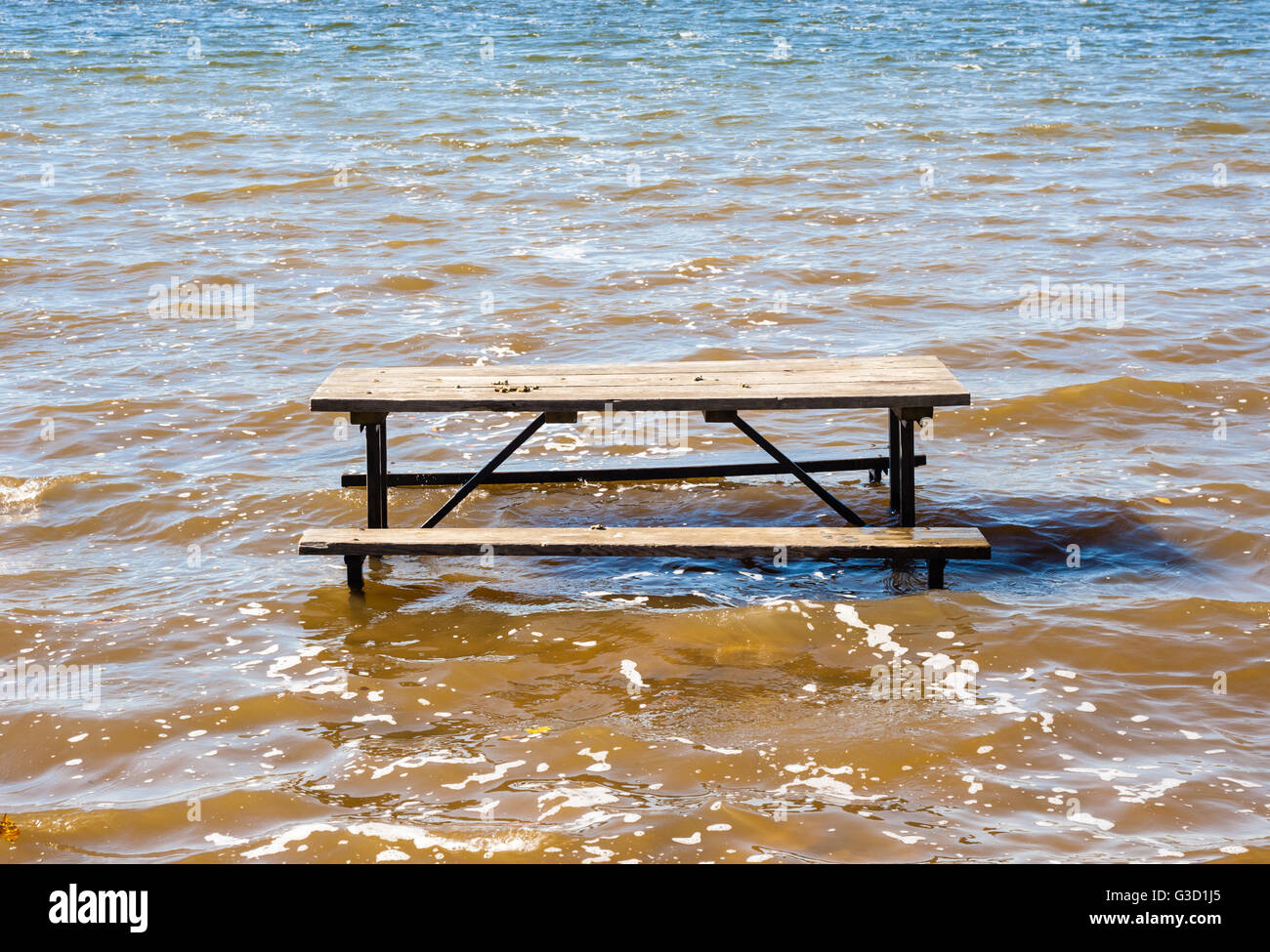 Svuotare tavolo da picnic che affonda nel fangoso ondulata acqua marrone. Foto Stock