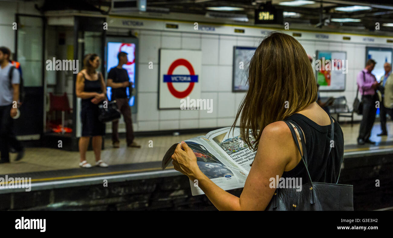 Donna che legge un giornale sulla piattaforma della stazione della metropolitana Victoria, mentre aspetta un treno, Londra, Regno Unito Foto Stock