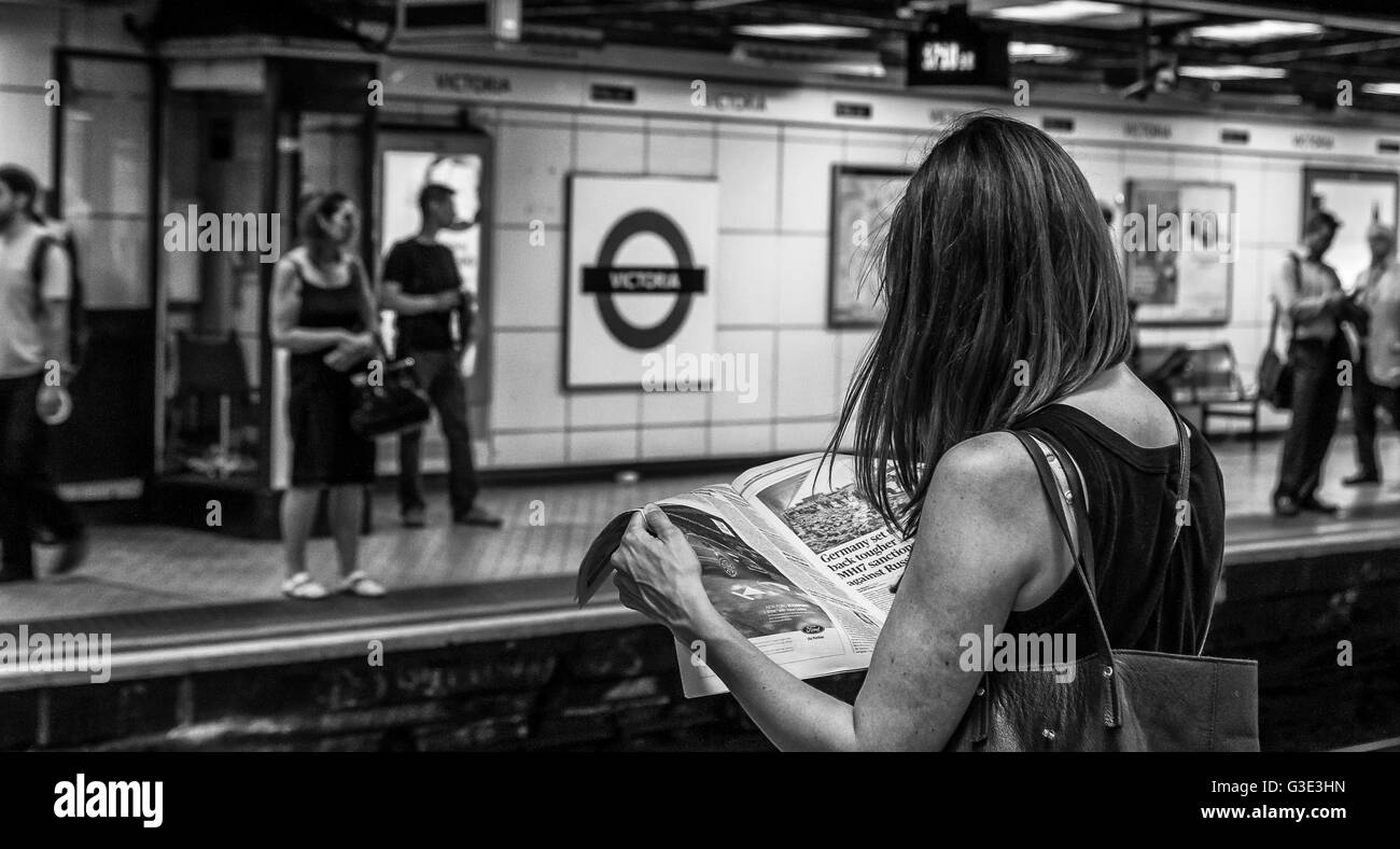 Donna che legge un giornale sulla piattaforma della stazione della metropolitana Victoria, mentre aspetta un treno, Londra, Regno Unito Foto Stock
