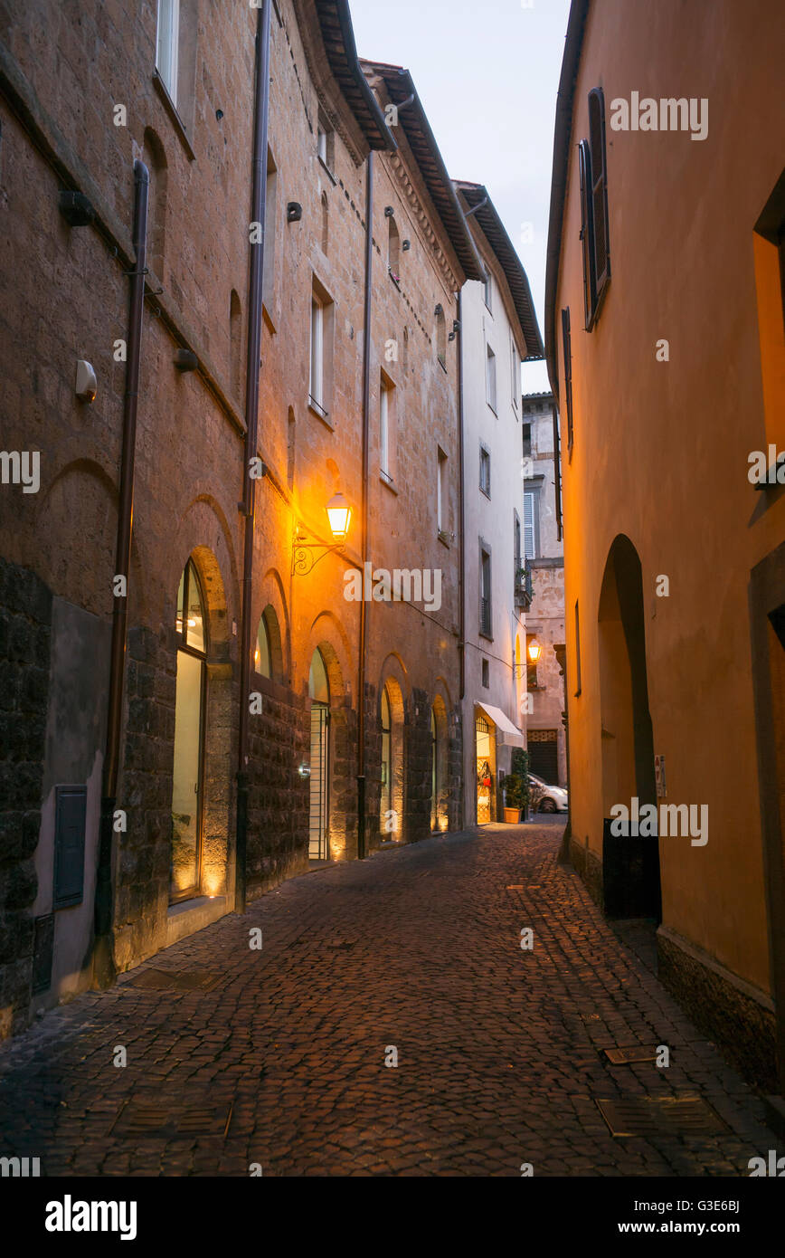 Una strada stretta tra gli edifici con una luce dorata illuminata al crepuscolo; Orvieto, Umbria, Italia Foto Stock