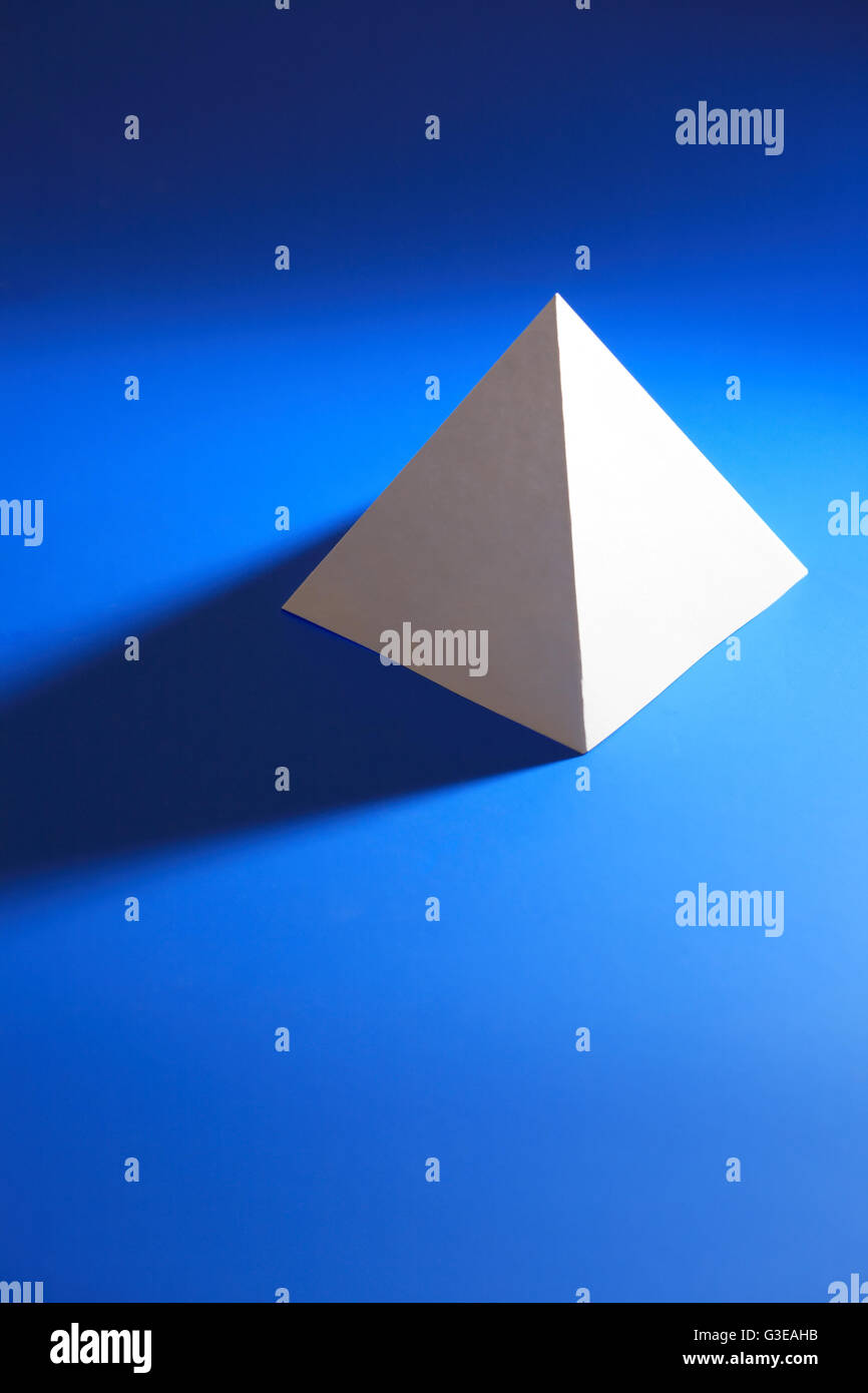 Concetto di geometria. Un white paper piramide su sfondo blu Foto Stock