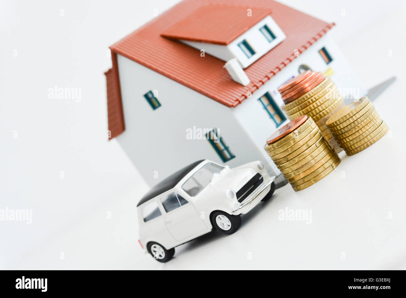 Auto e modello di casa con la pila di monete isolati su sfondo bianco Foto Stock