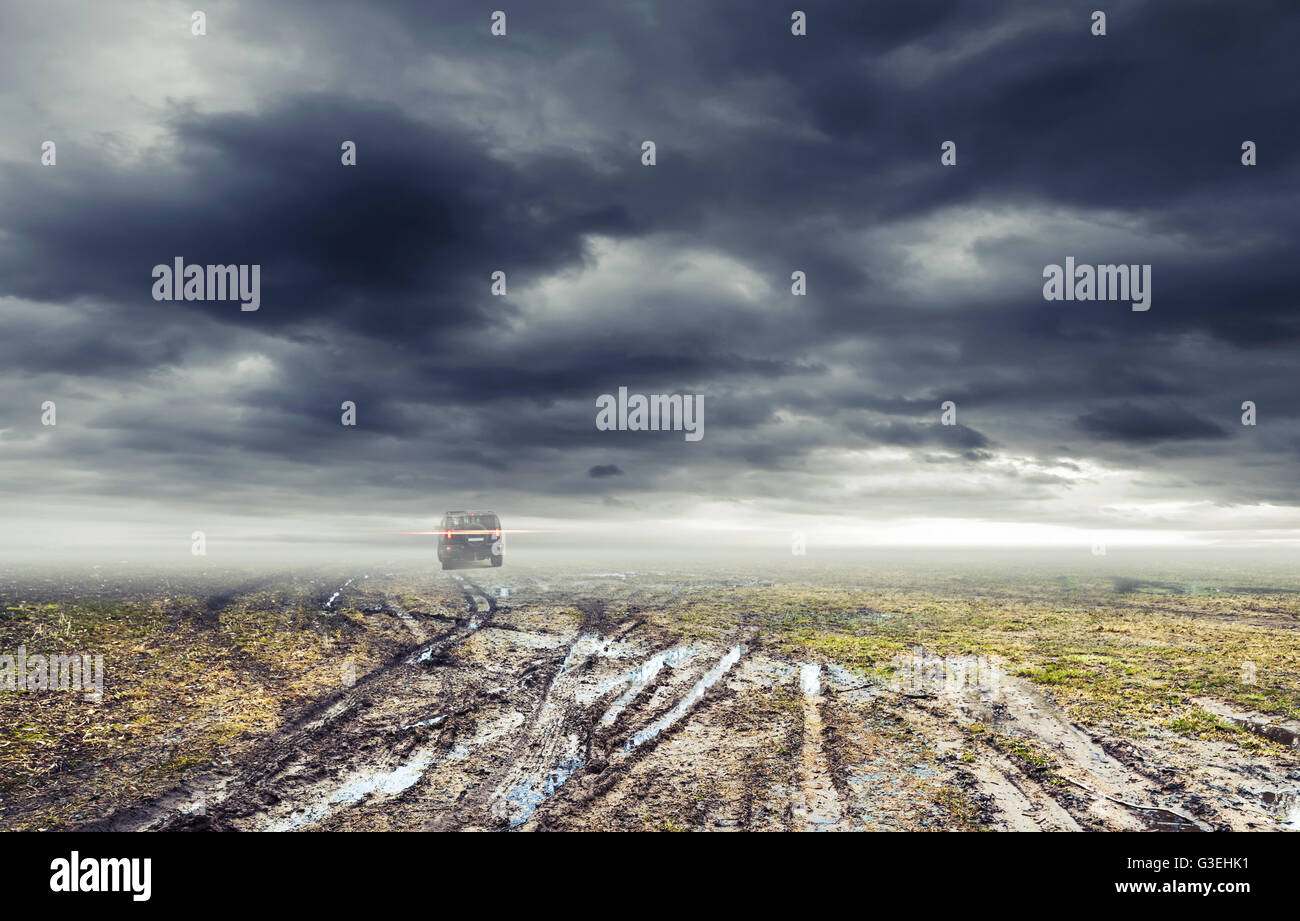 Sporco strada rurale con pozzanghere e fango al buio drammatico cielo tempestoso, SUV auto va lontano, sullo sfondo di trasporto Foto Stock