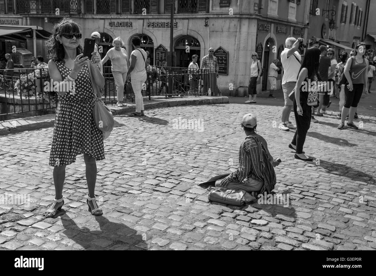 Un turista prende le foto in piedi accanto a un mendicante a Annecy, Haute-Savoie, Rhône-Alpes, in Francia Foto Stock