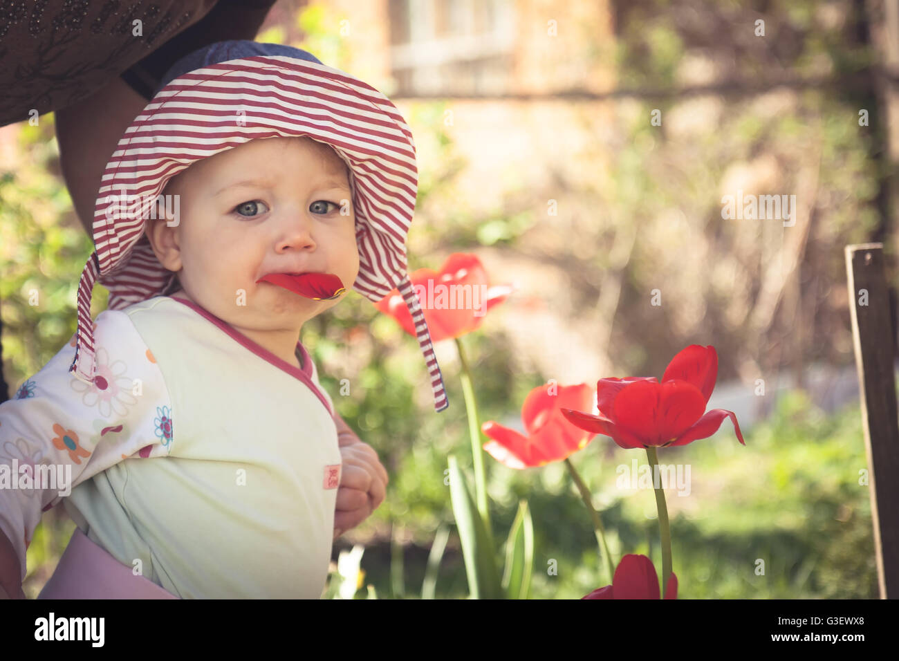 Funny Baby girl in panama hat passeggiate nel parco, tra i fiori di fioritura nella soleggiata giornata estiva con spazio di copia Foto Stock