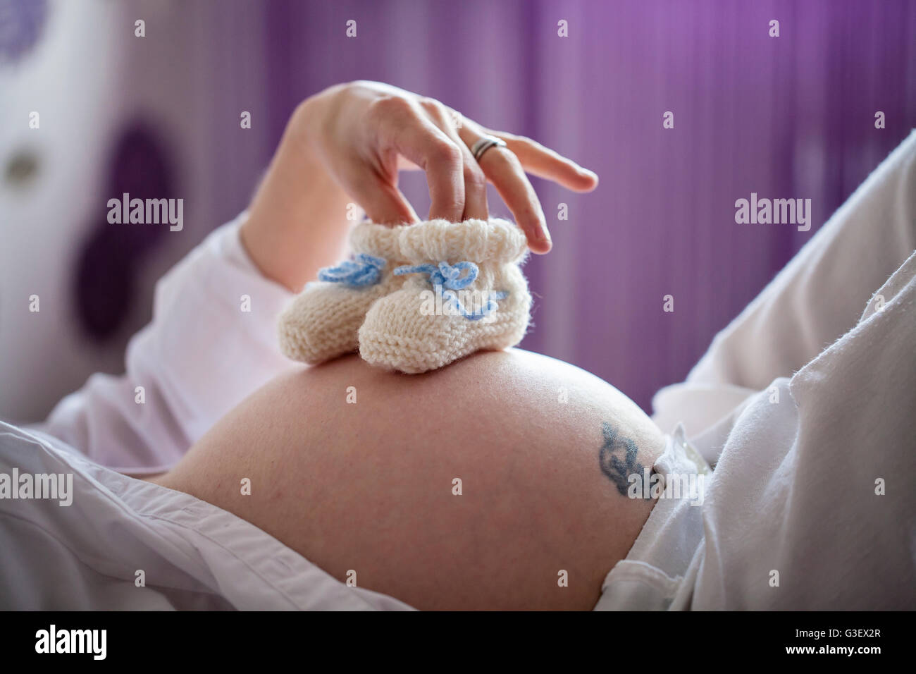 Donna incinta azienda scarpe per bambini sul suo ventre Foto Stock