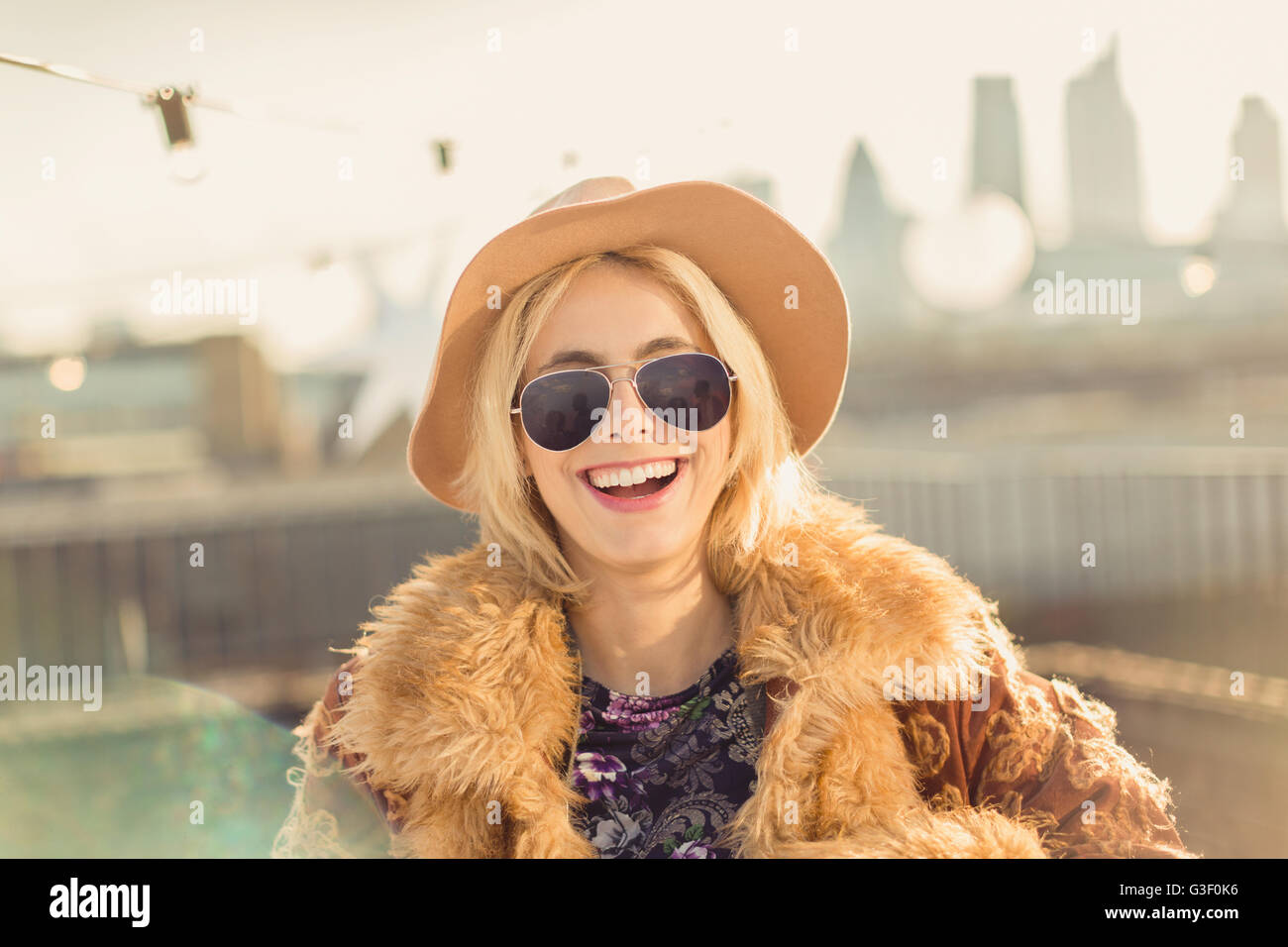 Ritratto entusiasta giovane donna che indossa un cappello e occhiali da sole sulla soleggiata terrazza sul tetto Foto Stock