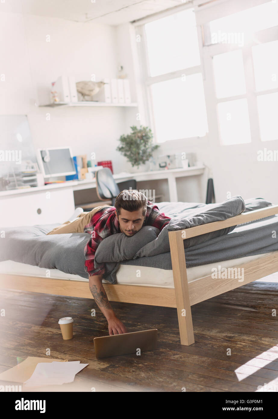 Giovane uomo posa sul letto tramite computer portatile in appartamento Foto Stock