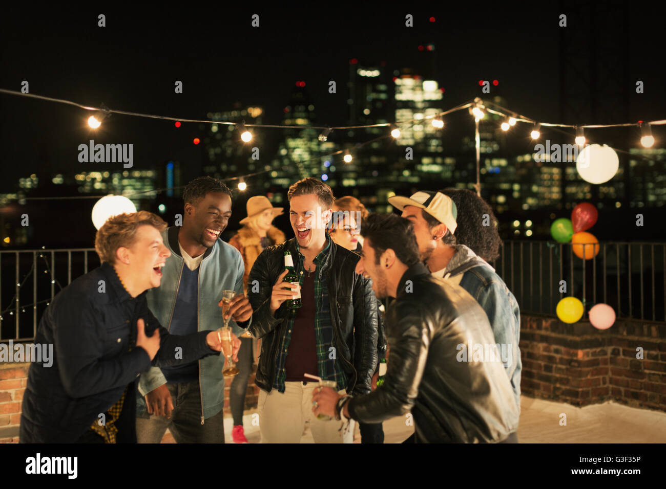 Giovani uomini di bere e ridere del partito sul tetto Foto Stock