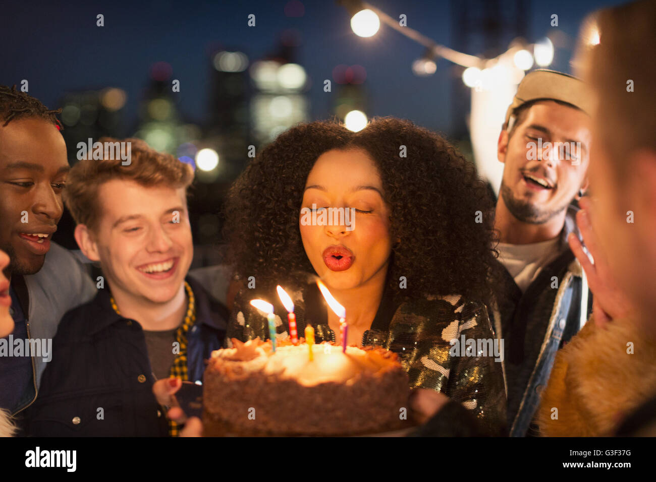 Amici tifo giovane donna che spegne le candeline sulla torta del compleanno Foto Stock