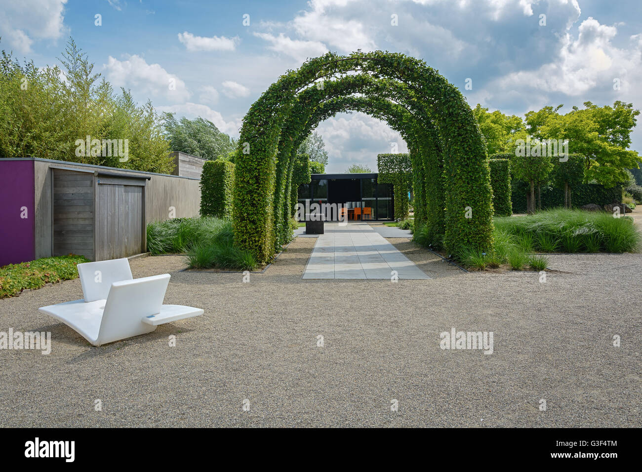 Un numero di archi telaio invaso dalle liane con di fronte 2 white alla moda di sedie da giardino Foto Stock
