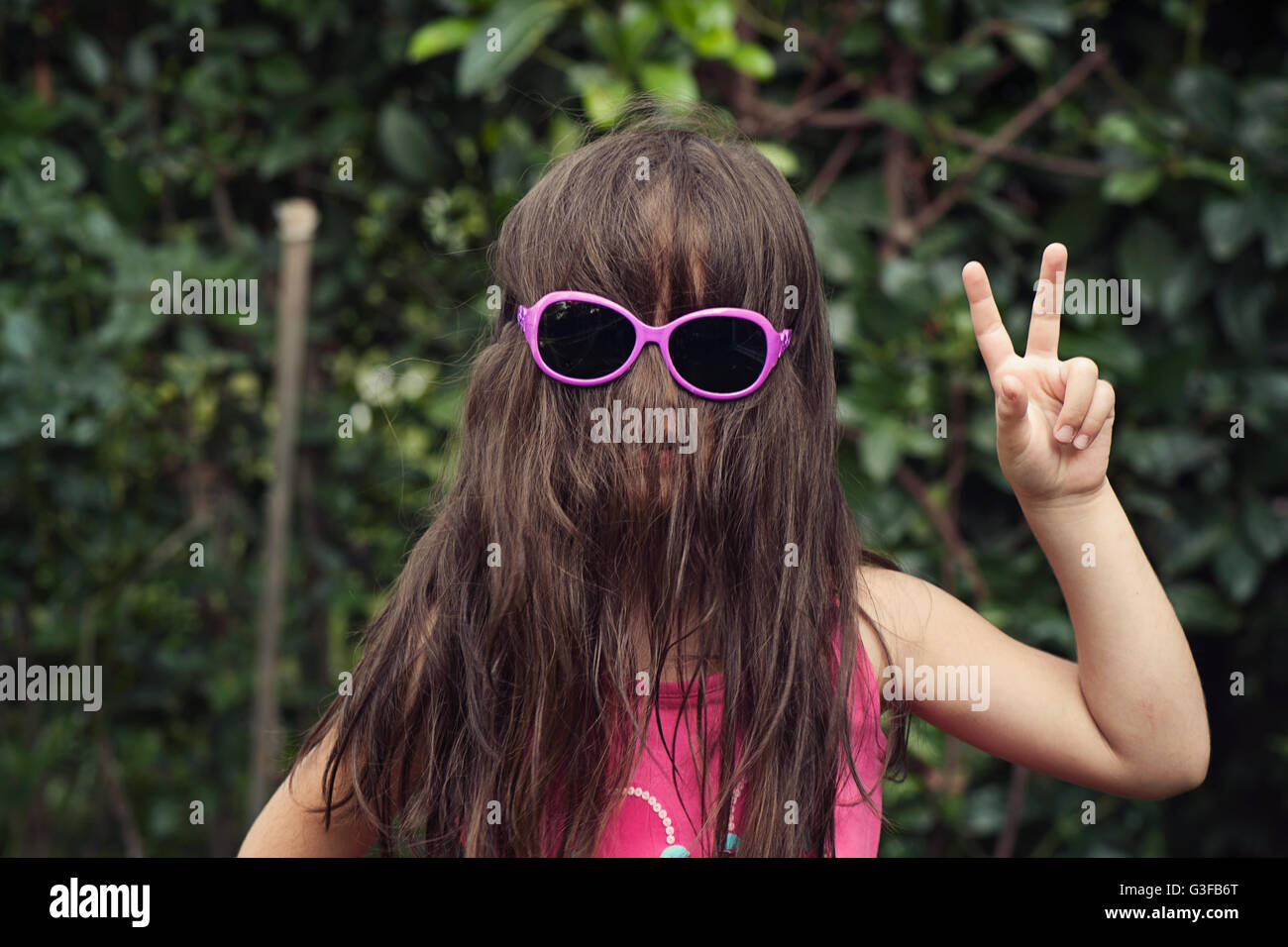 Piccola ragazza con i capelli sulla faccia indossando occhiali da sole,che mostra un segno di pace Foto Stock