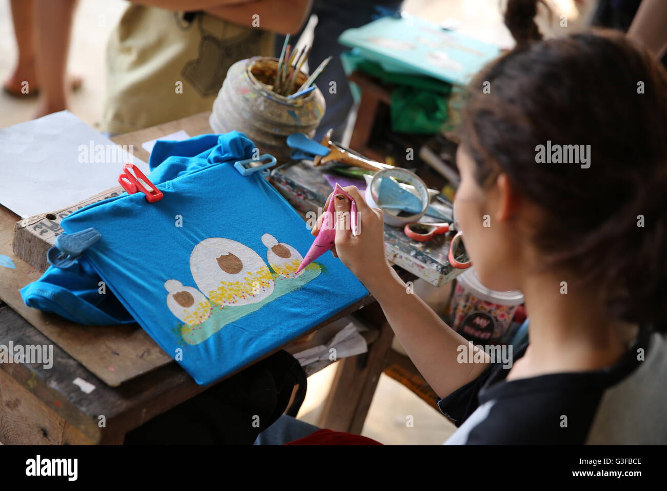 Donna che utilizza vernici acriliche per creare un'immagine di pecora su una t-shirt Foto Stock