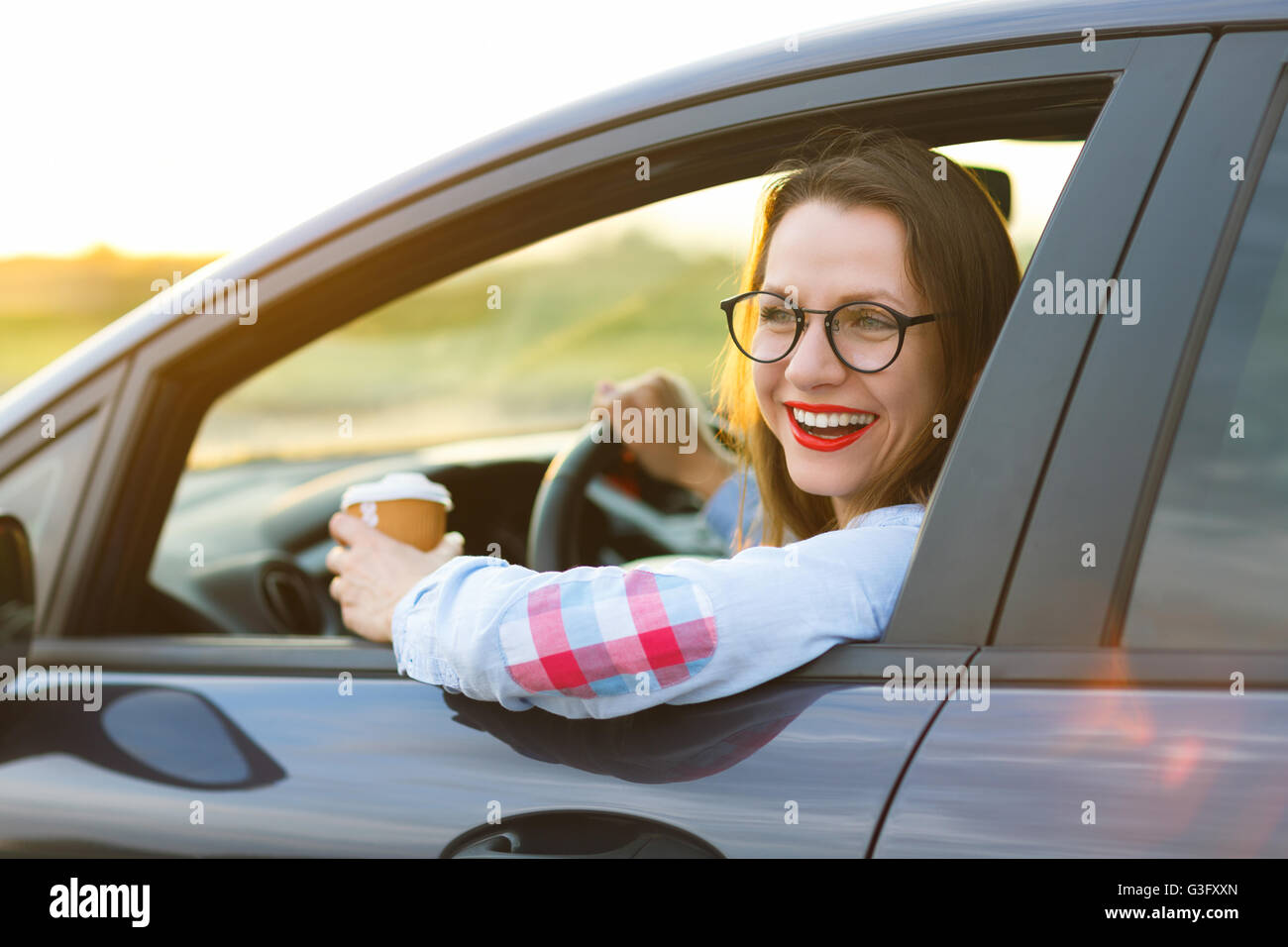 Felice giovane donna con il caffè per andare alla guida la sua automobile Foto Stock