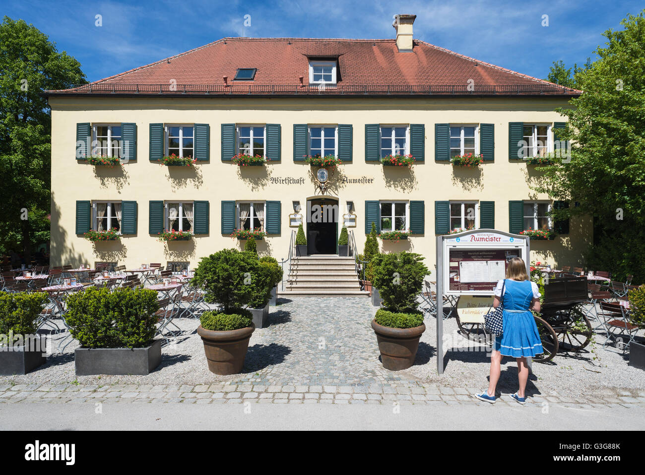 Donna in abito bavarese leggendo il menu all'esterno del ristorante Aumeister nel Giardino Inglese, Monaco di Baviera, Germania Foto Stock