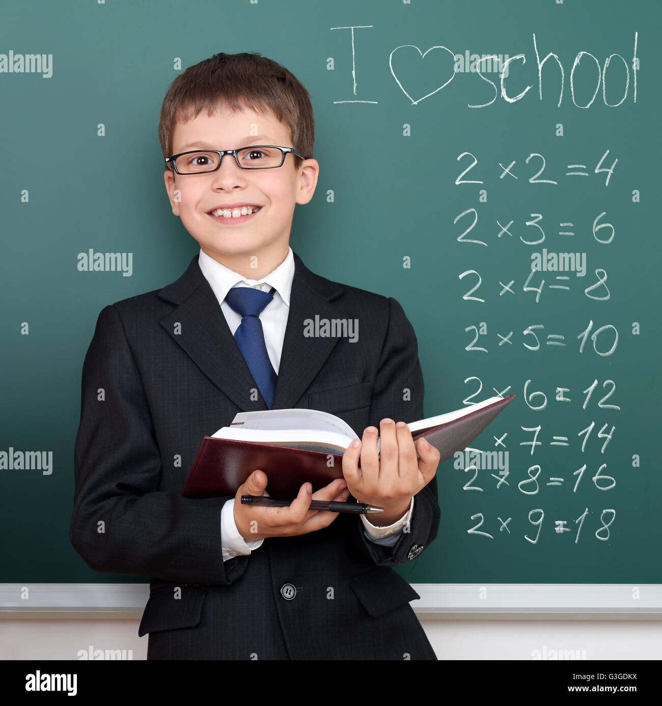 Scuola Ragazzo con libro ritratto su sfondo lavagna, io amo la scuola testo con esercizi di matematica, vestito in classico abito nero, ed. Foto Stock