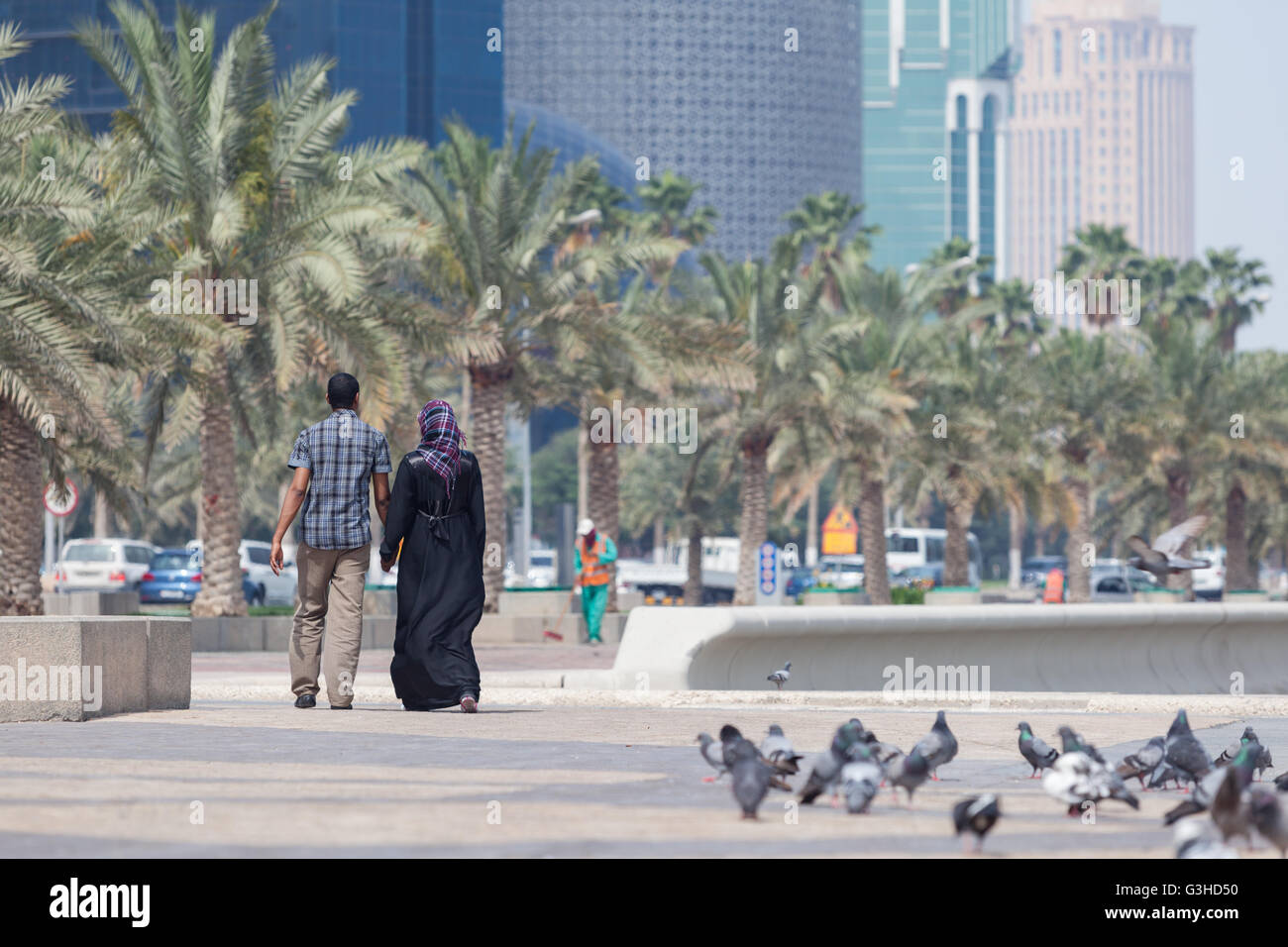 Uomo e donna che cammina su Al Corniche, West Bay, a Doha. Donna in Abaya. Lavoratore in background. Foto Stock