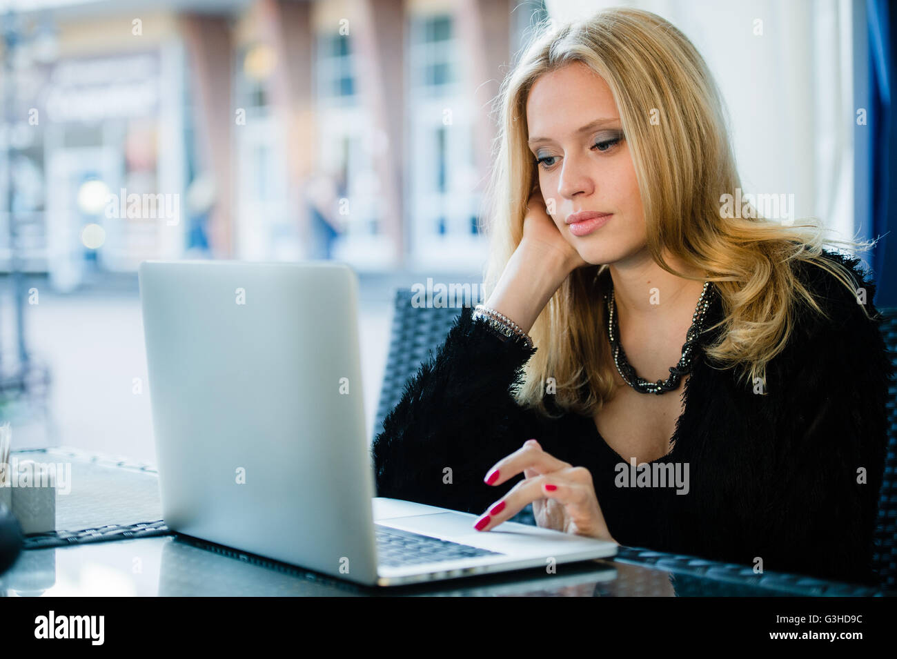 Giovane donna gorgeous di bere il caffè seduti con open computer laptop all'aperto, femmina freelancer lavorando sul notebook in un cafè sul marciapiede, graziosa ragazza studente navigando in rete al di fuori sulla terrazza Foto Stock