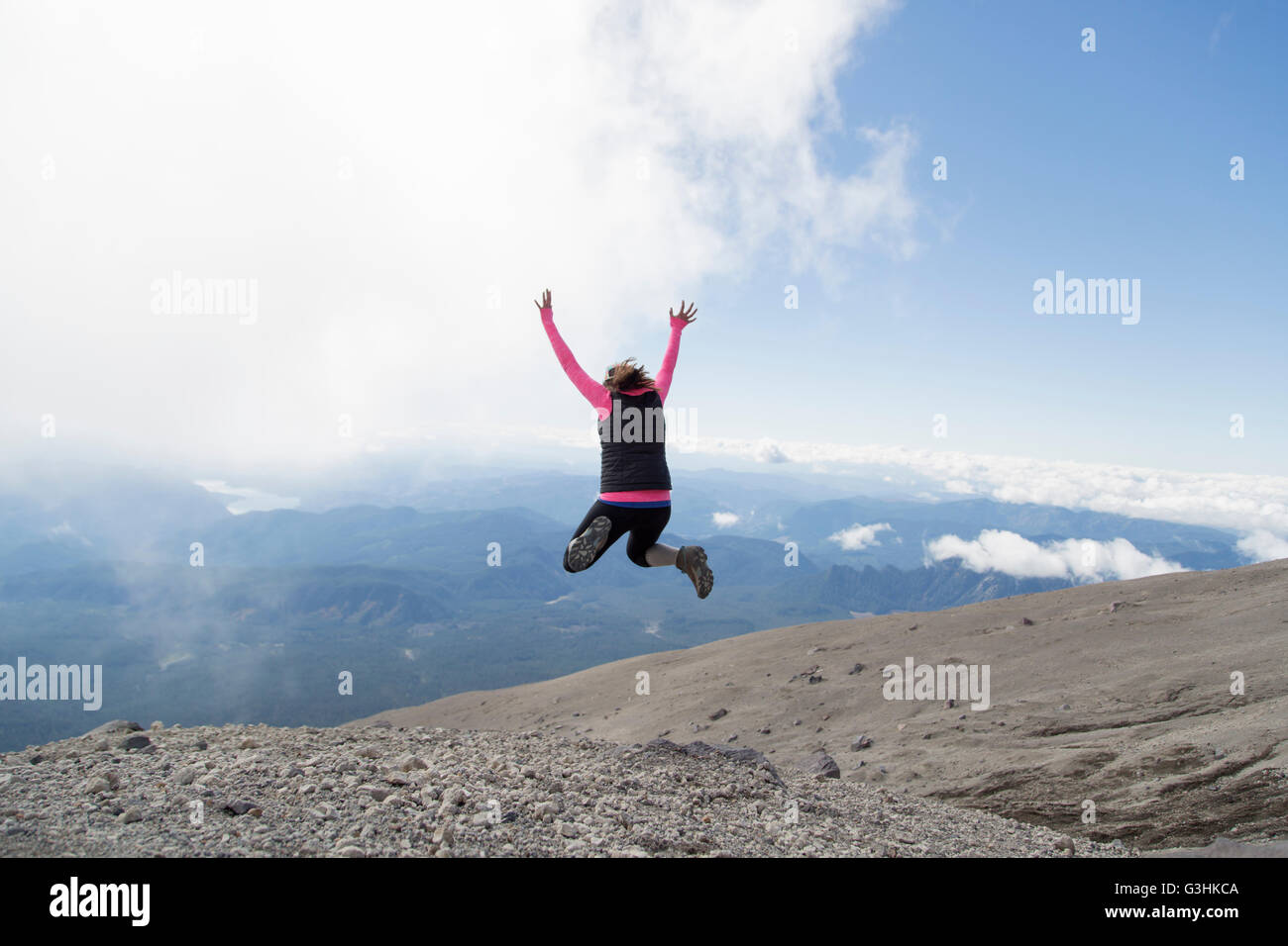 Giovane donna alla cima della montagna, saltando fro gioia, vista posteriore, Mt. Sant Helens, Oregon, Stati Uniti d'America Foto Stock