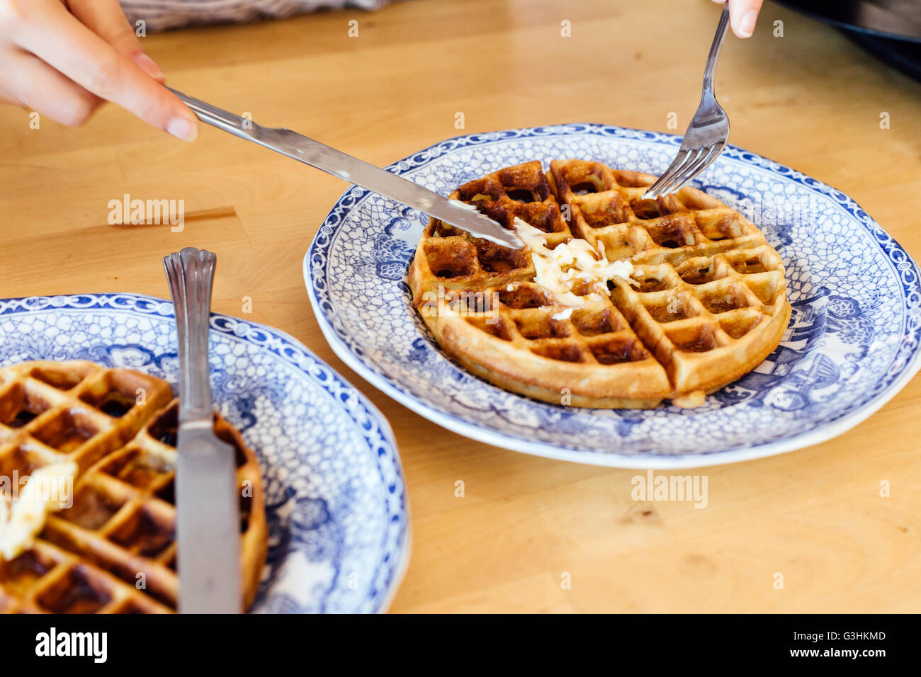 Vista ritagliata della mano womans diffondere il burro su cialde fresche Foto Stock