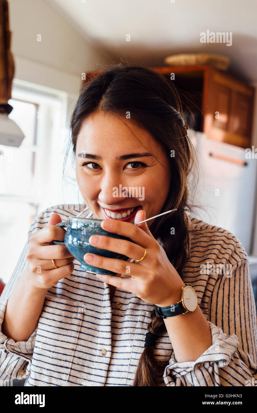 Donna che mantiene tazza da tè la bocca a guardare fotocamera a sorridere Foto Stock