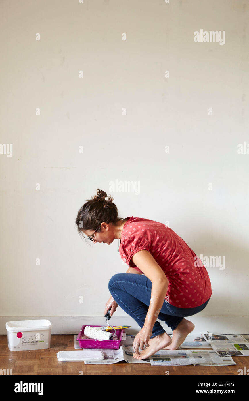 Donna in ginocchio, immergendo il rullo di vernice in paint Foto Stock