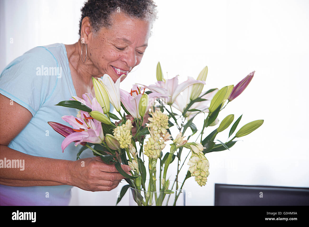 Senior donna odore di vaso di fiori, sorridente Foto Stock