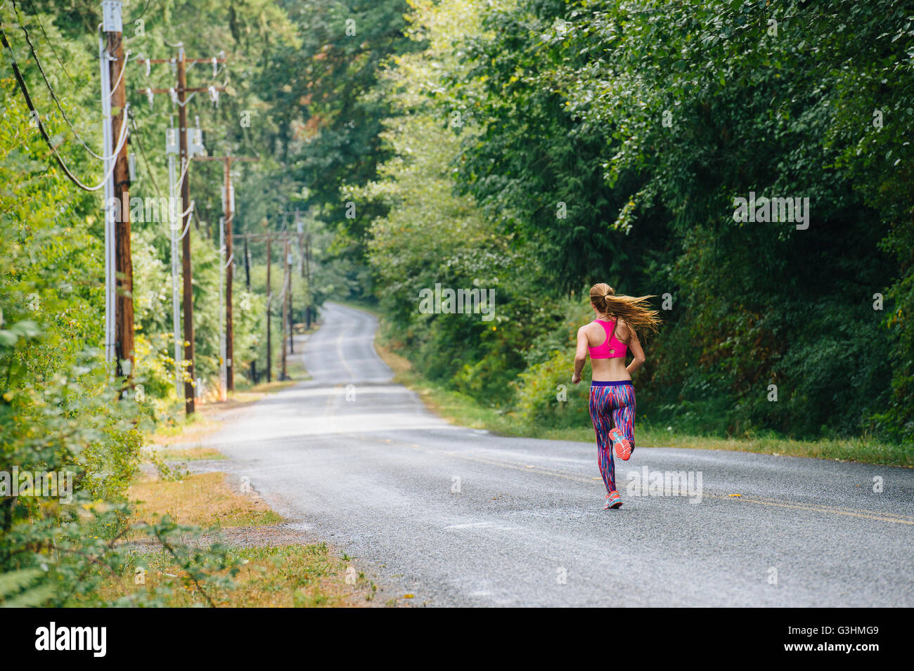 Vista posteriore del femminile adolescente runner correndo giù per strada rurale Foto Stock