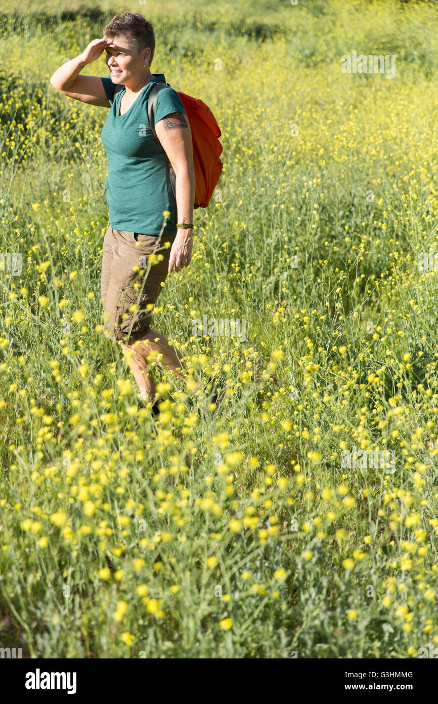 Donna escursionista nel prato di fiori selvaggi schermare gli occhi guardando lontano Foto Stock