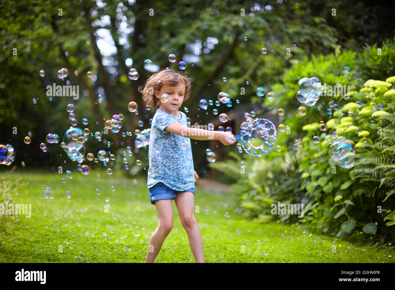 Ragazza sventolare bubble wand e rendendo le bolle in giardino Foto Stock