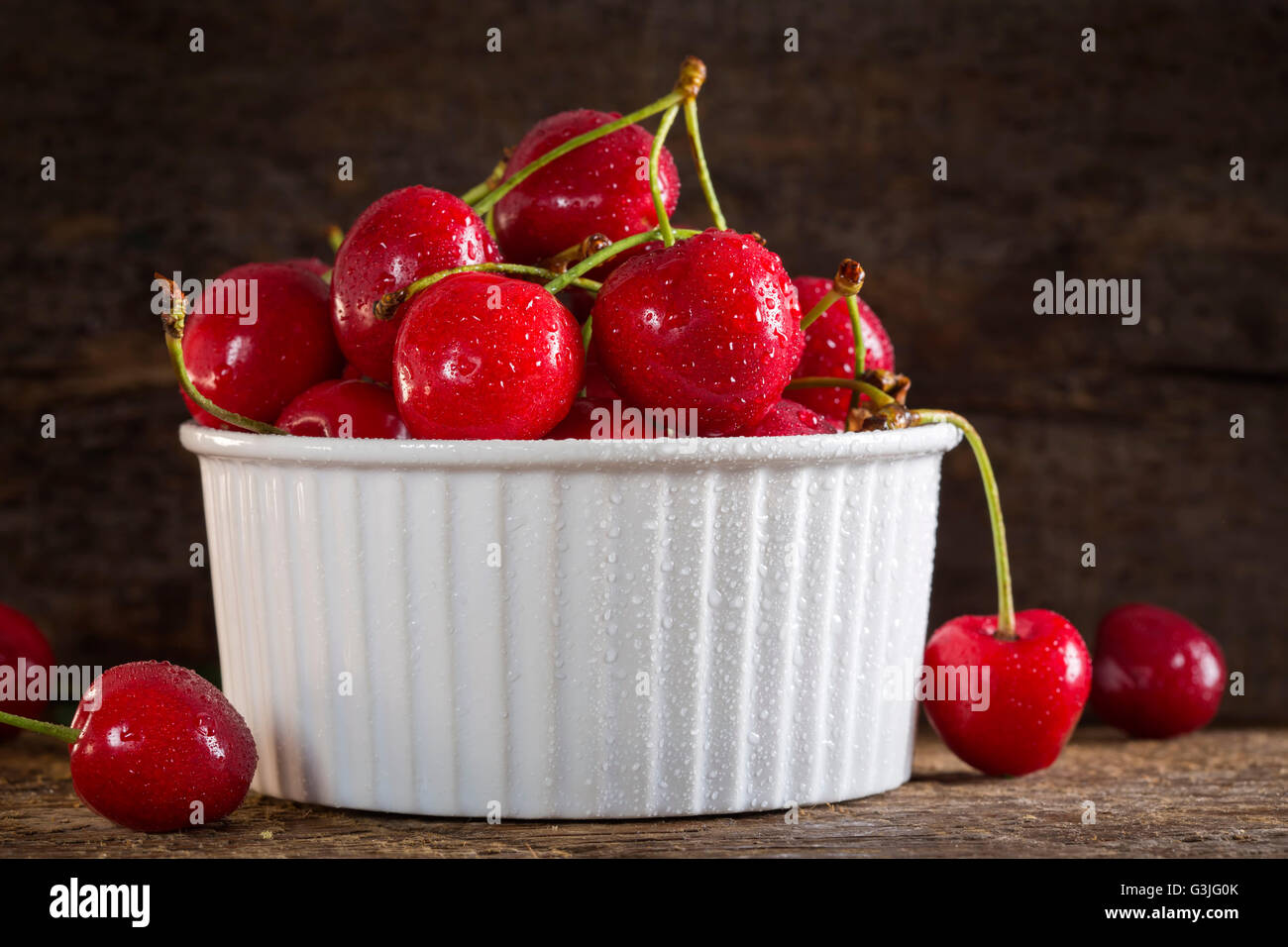 Ciotola bianco con fresche ciliege rosse su rustico sfondo di legno Foto Stock