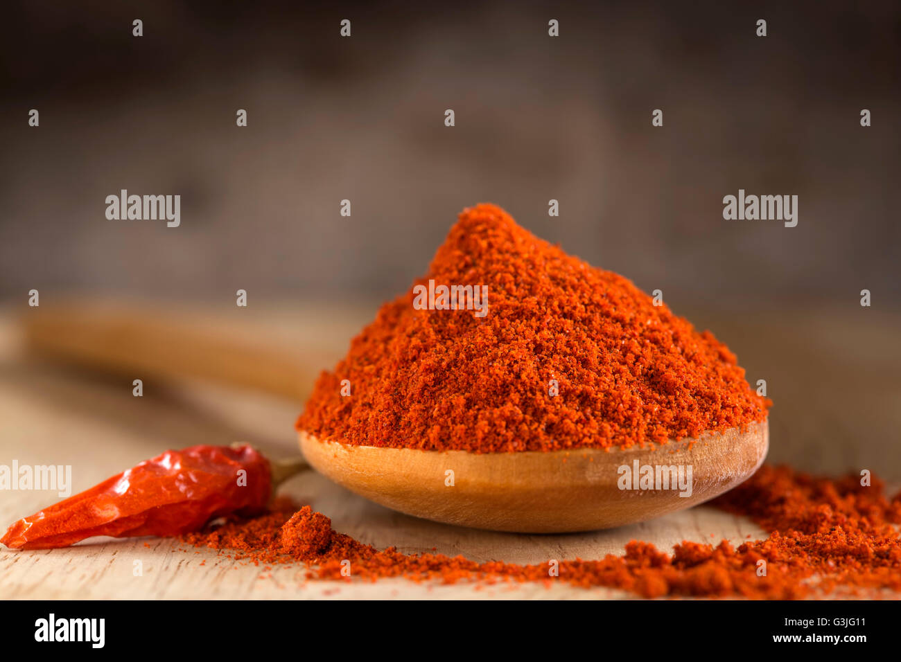 Cucchiaio riempito con red hot paprika in polvere e peperoncino rosso su sfondo di legno Foto Stock