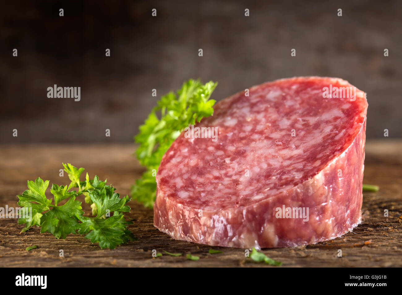 Pezzo di fresco salame italiano sulla tavola di legno con erbe aromatiche Foto Stock