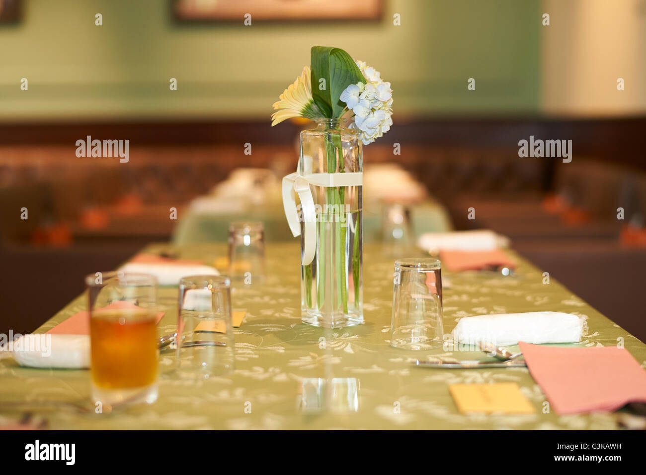 Un piccolo vaso di vetro di fiori bianchi su un tavolo verde ad un ricevimento di nozze. Foto Stock