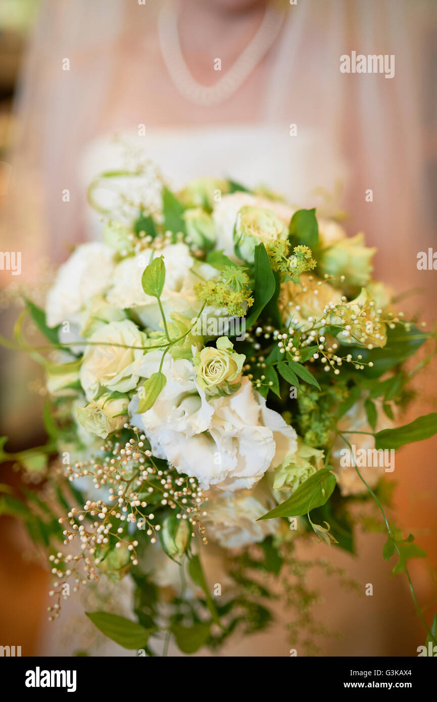 Un colpo di una sposa dal collo in giù al di fuori della messa a fuoco in possesso di un colore bianco e verde bouquet di fiori. Foto Stock