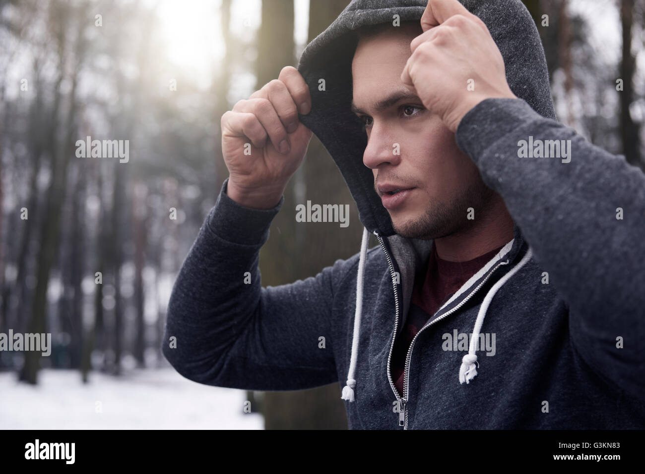 Giovane uomo che indossa felpa con cappuccio, in presenza di neve, il paesaggio rurale Foto Stock