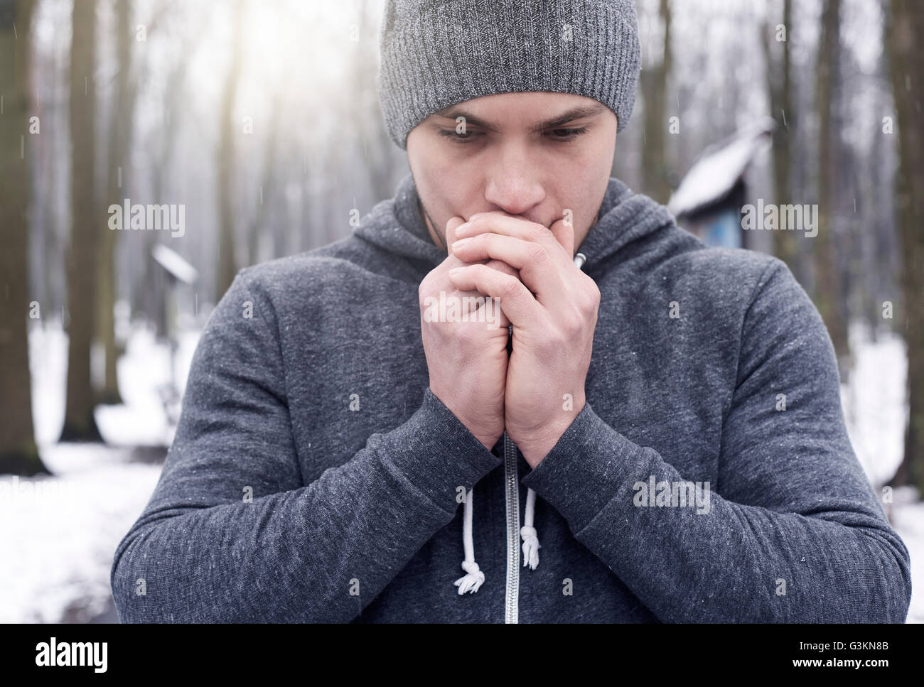 Giovane uomo sulla respirazione mani, in boschi innevati Foto Stock