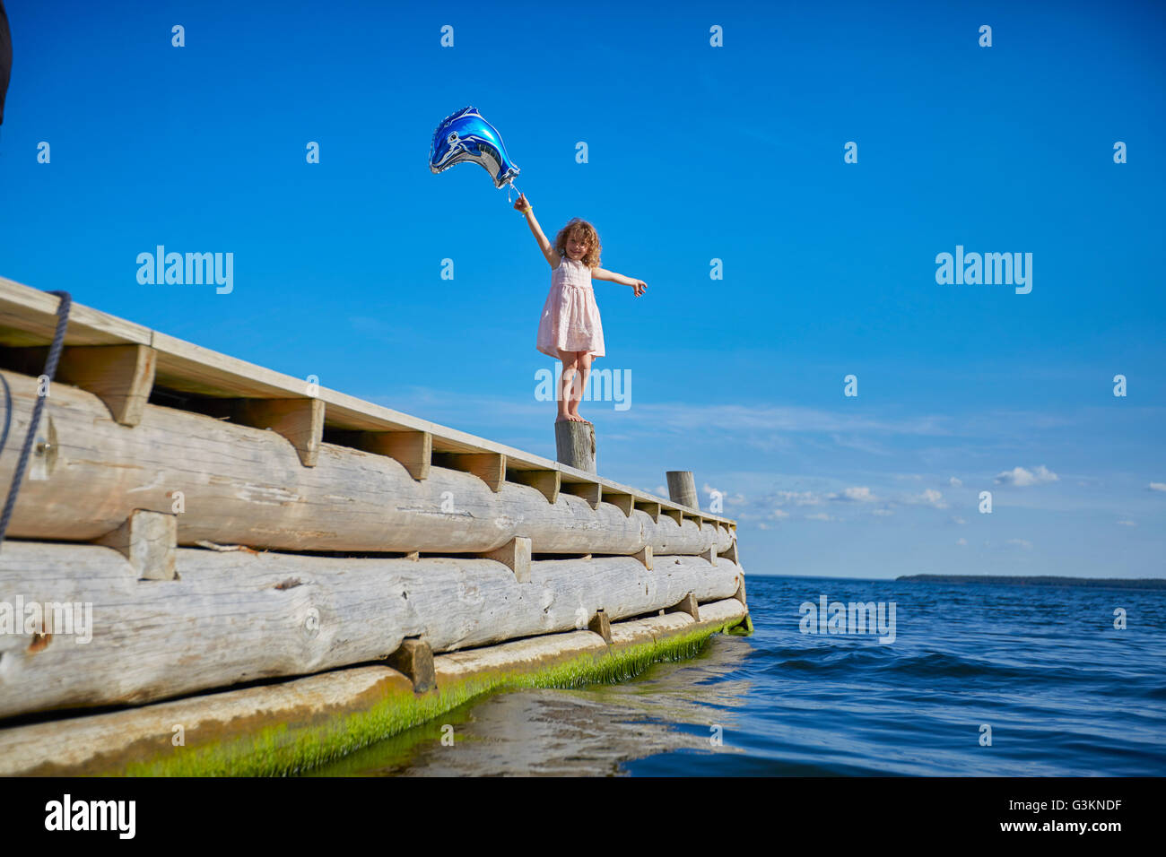 Giovane ragazza in piedi sul palo di legno sul molo, tenendo palloncino elio Foto Stock