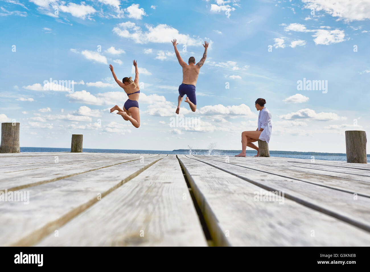 Giovane donna seduta sul post sul molo in legno, guardare gli amici che saltano in mare Foto Stock