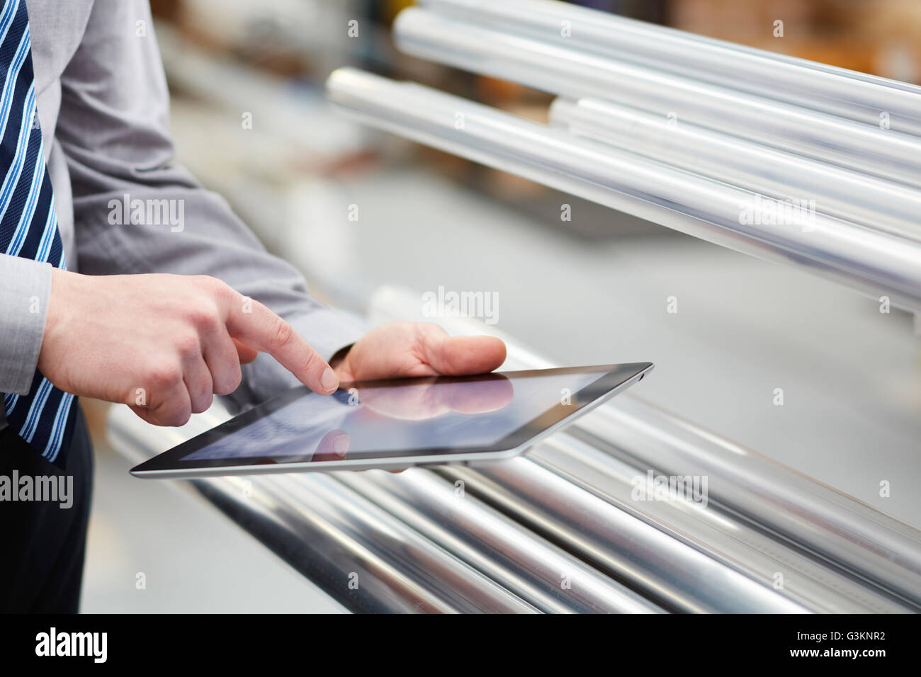Close up di lavoratore stock tenendo le aste metalliche con tavoletta digitale touchscreen nella tenda a rullo factory Foto Stock