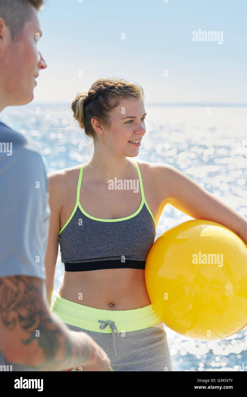 Donna di fronte oceano tenendo palla gialla che guarda lontano sorridente Foto Stock