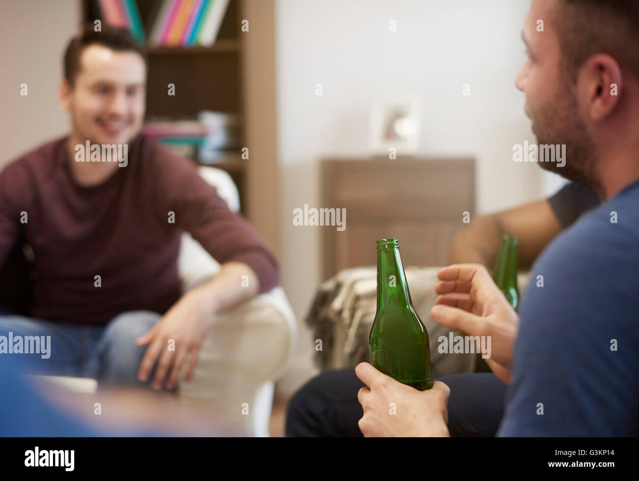 Un gruppo di uomini in seduta lounge tenendo le bottiglie di birra in chat Foto Stock