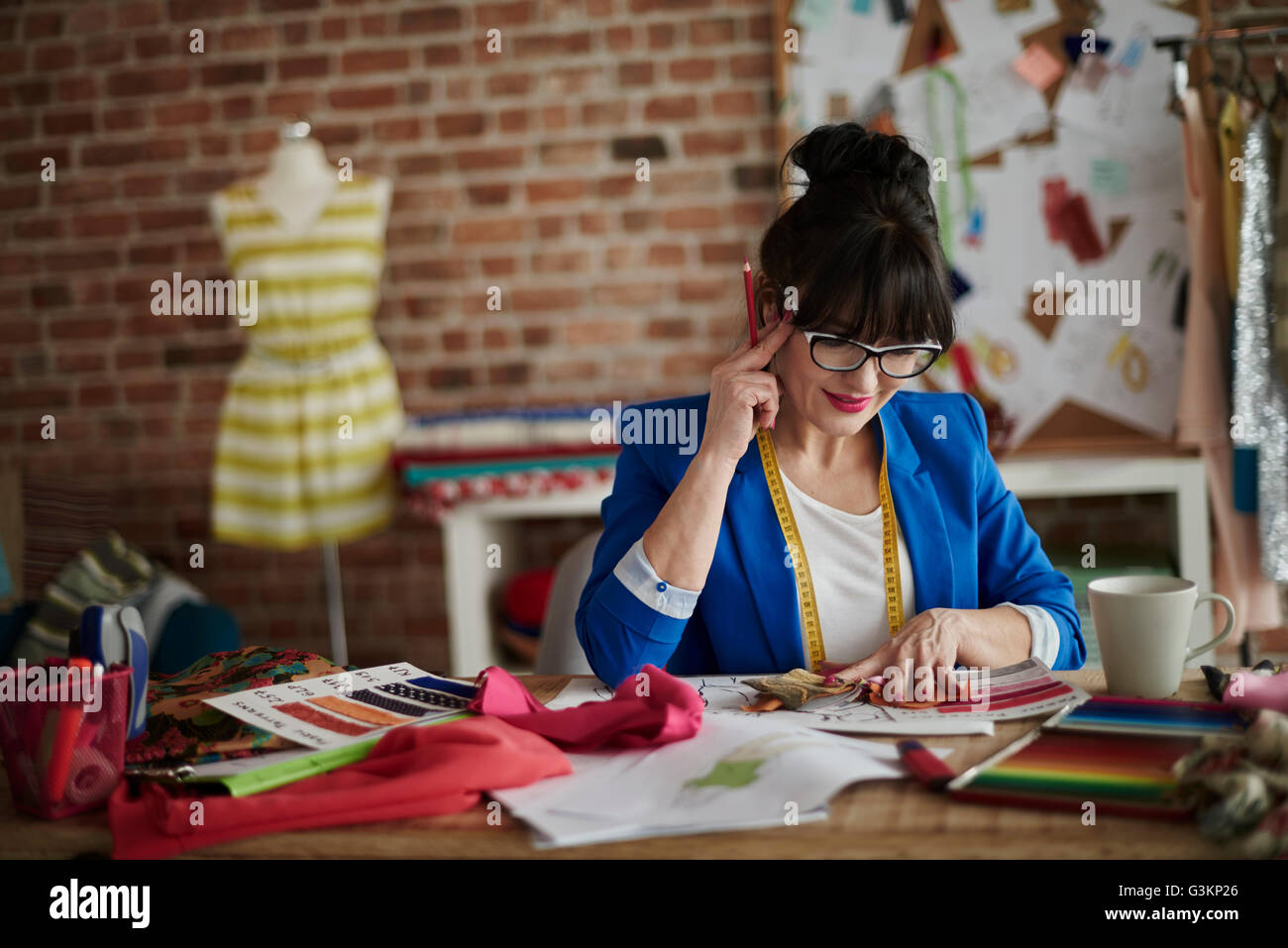 La donna nel design studio seduto alla scrivania, mano sulla testa guardando verso il basso Foto Stock