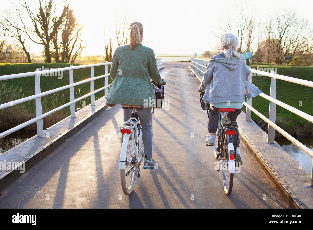 Vista posteriore delle donne ciclismo biciclette sul ponte che attraversa il fiume Foto Stock