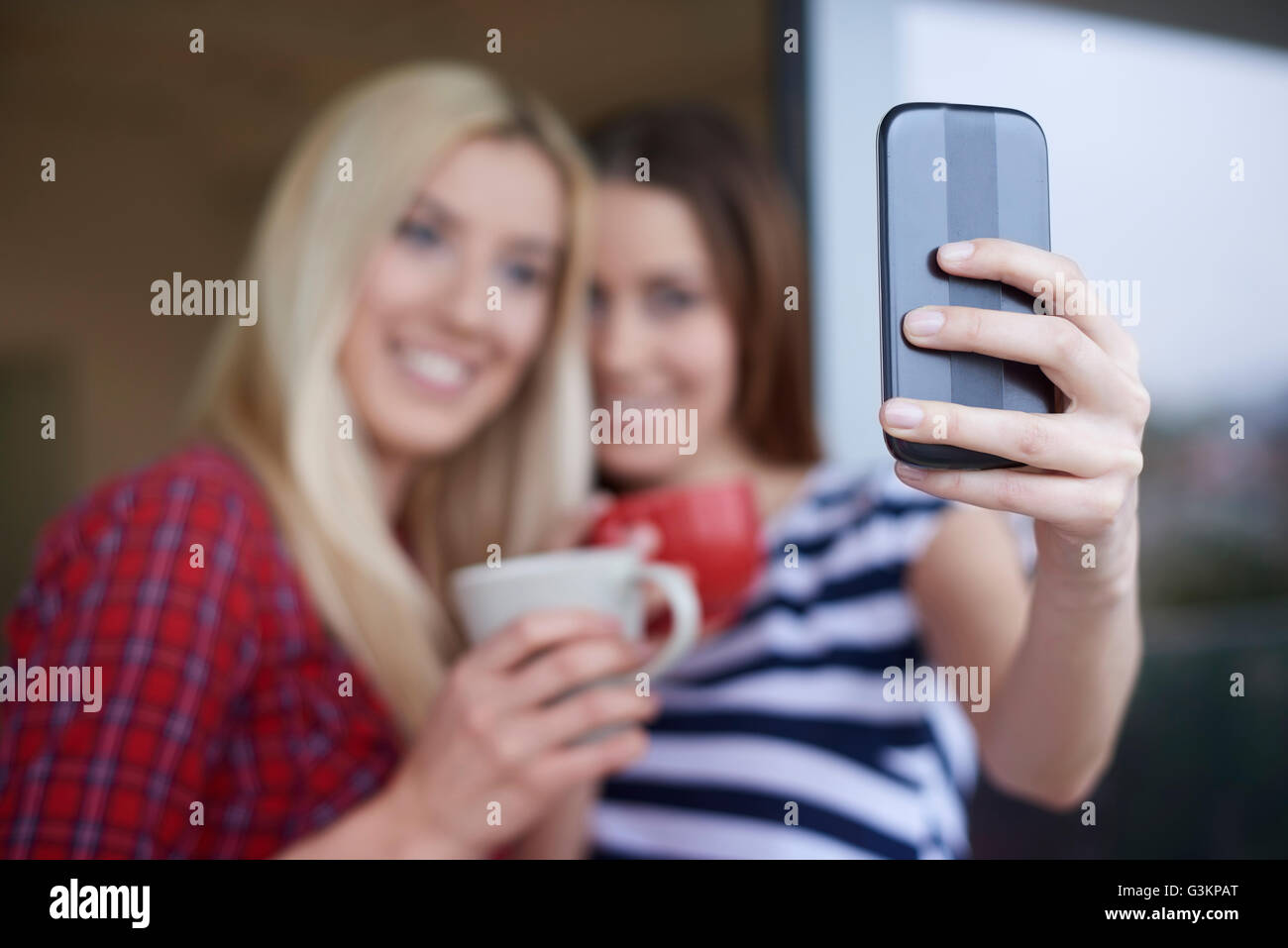 Due amiche, bere il caffè all'aperto, tenendo autoritratto utilizza lo smartphone Foto Stock