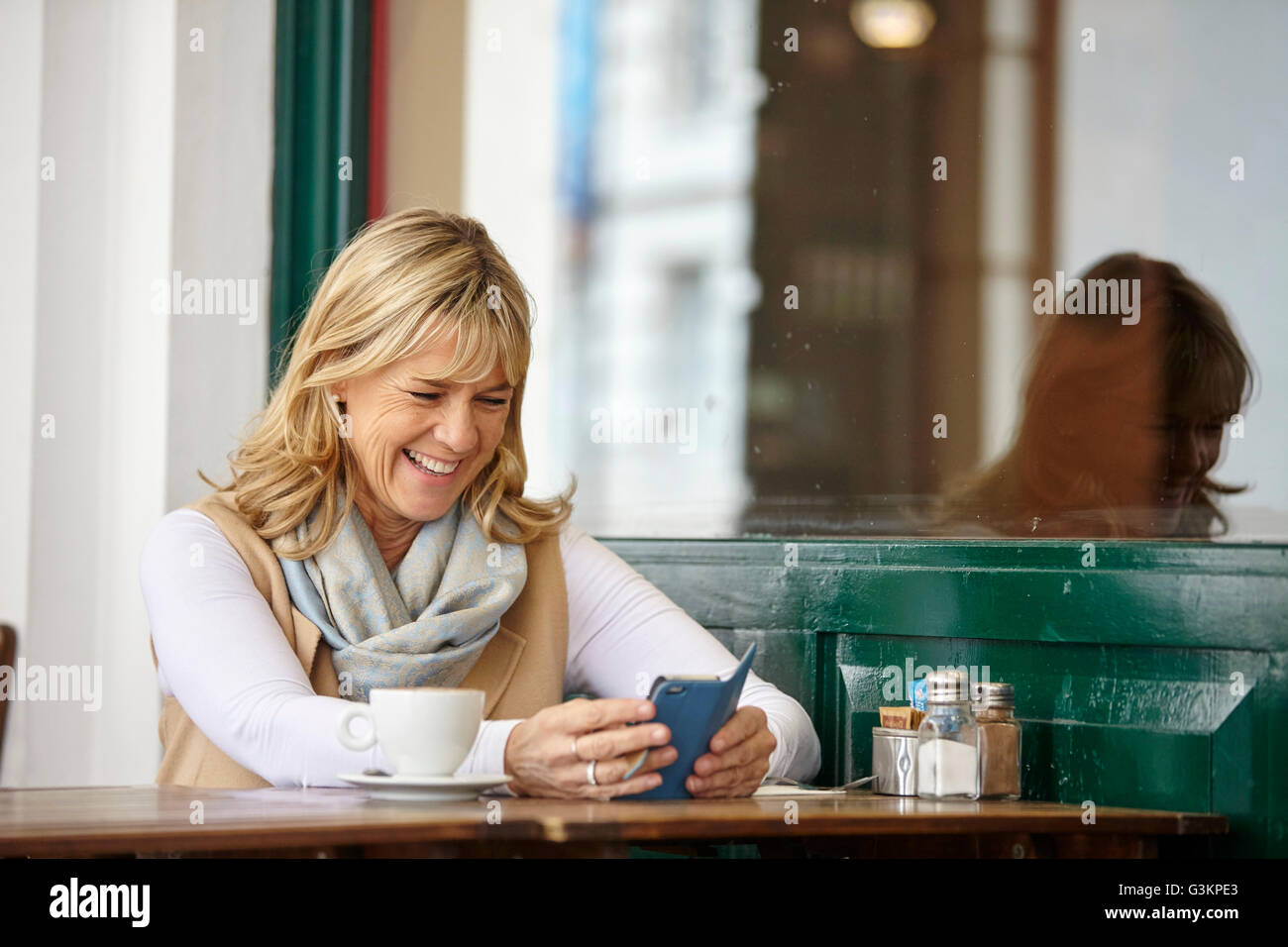 Donna matura la lettura del testo dello smartphone al cafè sul marciapiede tabella Foto Stock