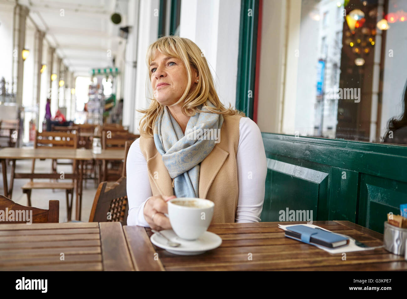 Donna matura guardando fuori dal cafè sul marciapiede tabella Foto Stock