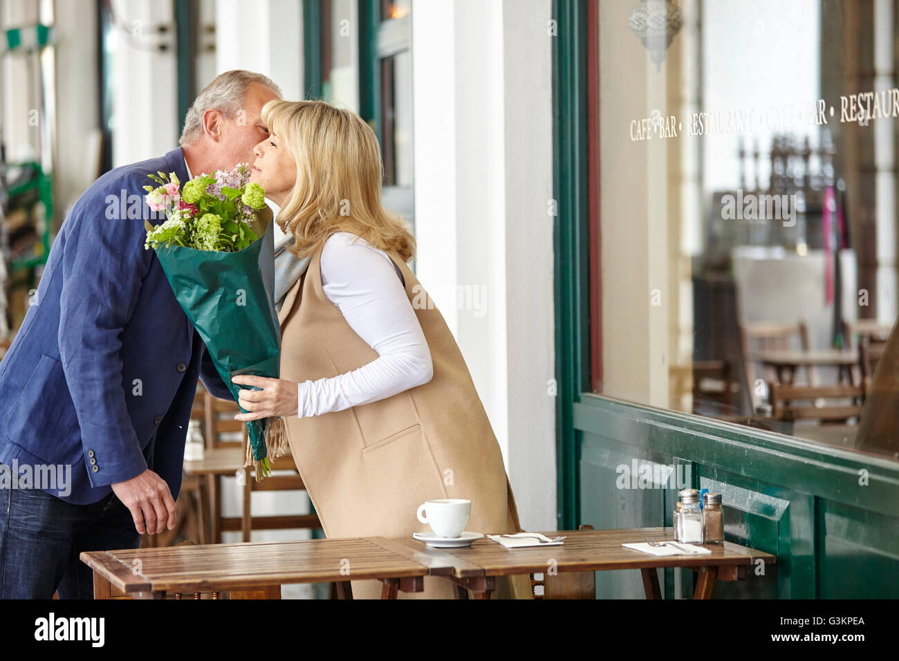 Uomo maturo kissing data sulla guancia al cafè sul marciapiede tabella Foto Stock