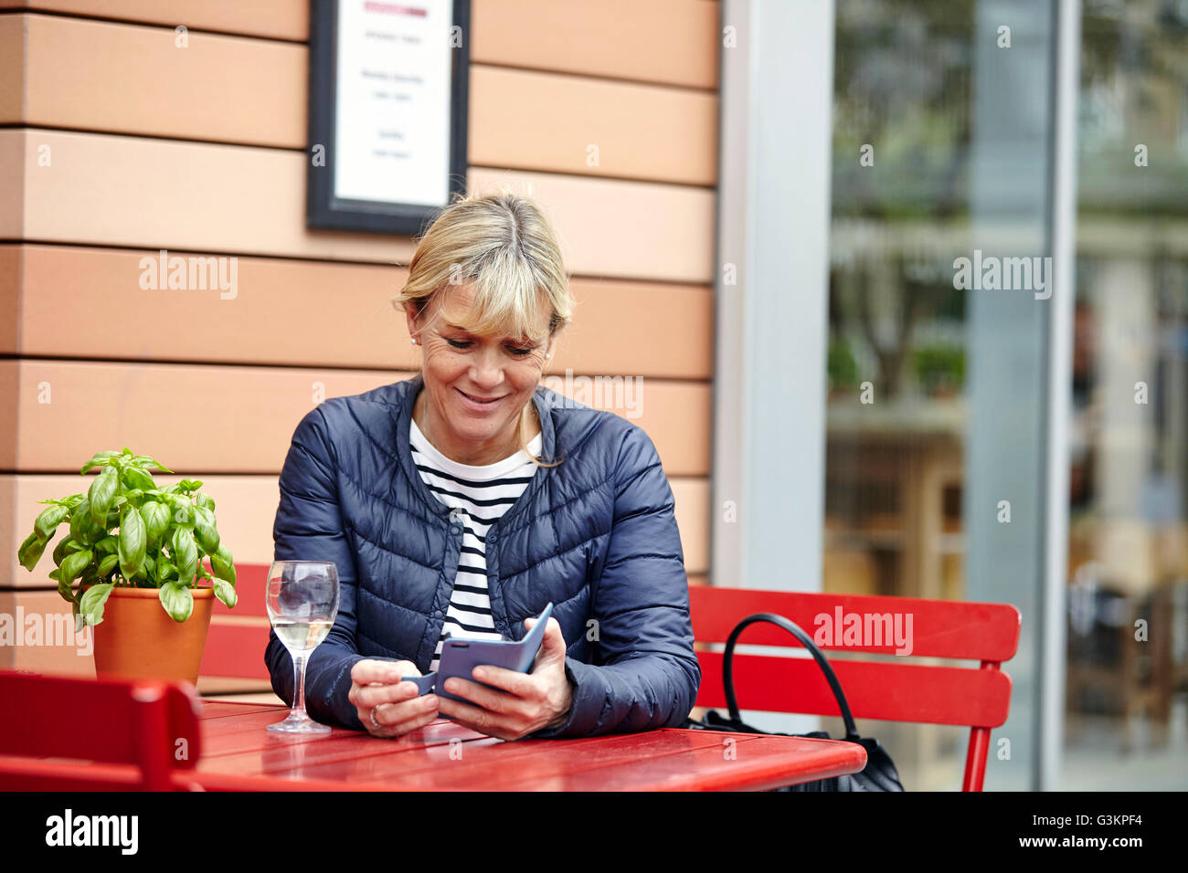 Donna matura la lettura di testi di smartphone a sidewalk cafe Foto Stock