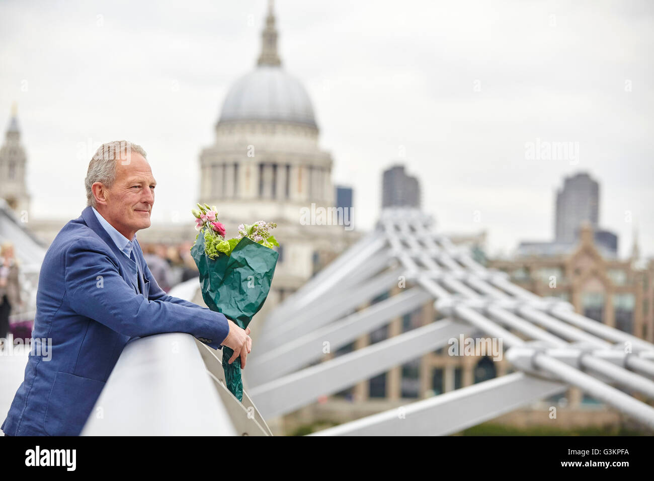 Uomo maturo con bouquet in attesa sul Millennium Bridge, London, Regno Unito Foto Stock